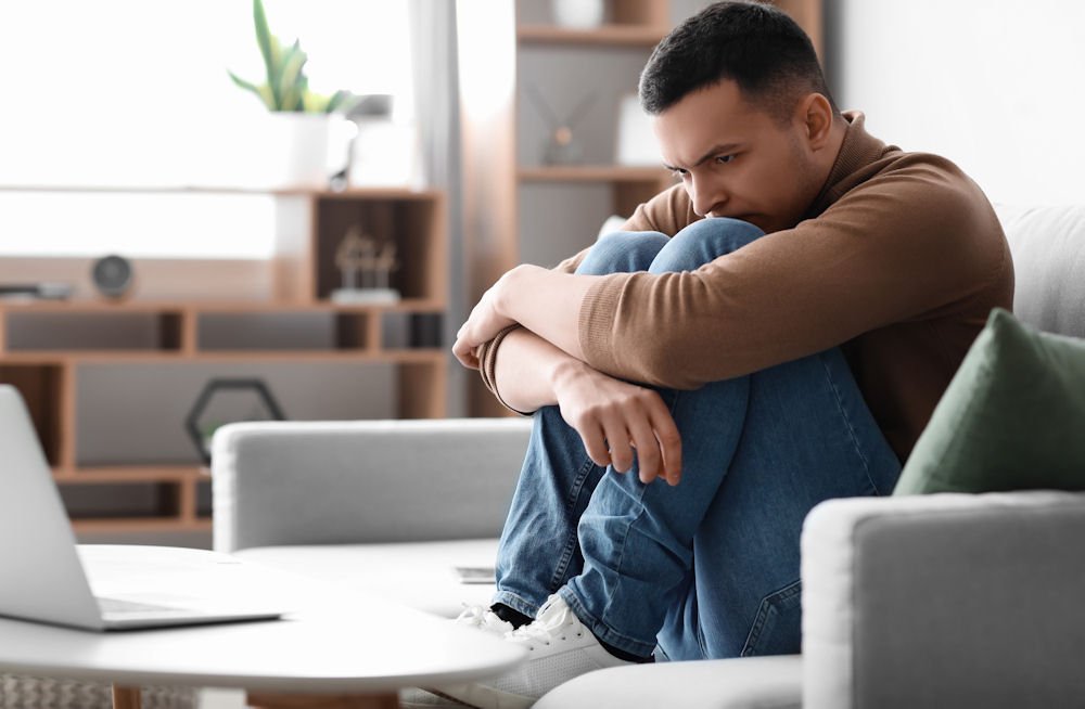 man sitting on a couch appearing stressed and suffering anxiety